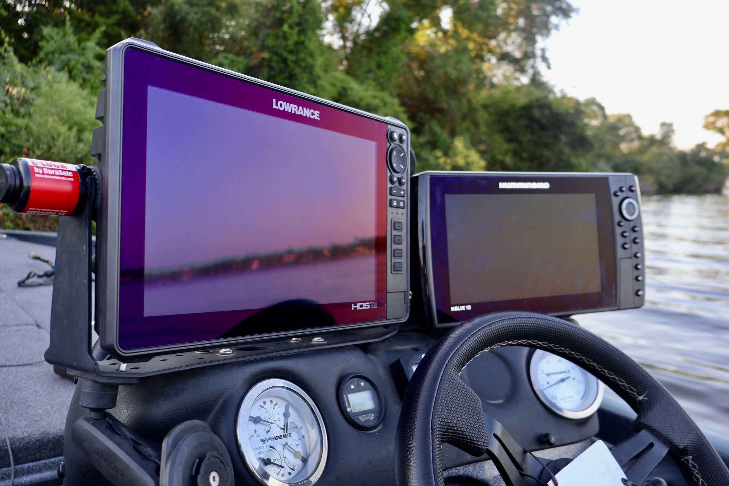 Fishing boat dashboard featuring Lowrance fishfinders and gauges with serene water view in the background.