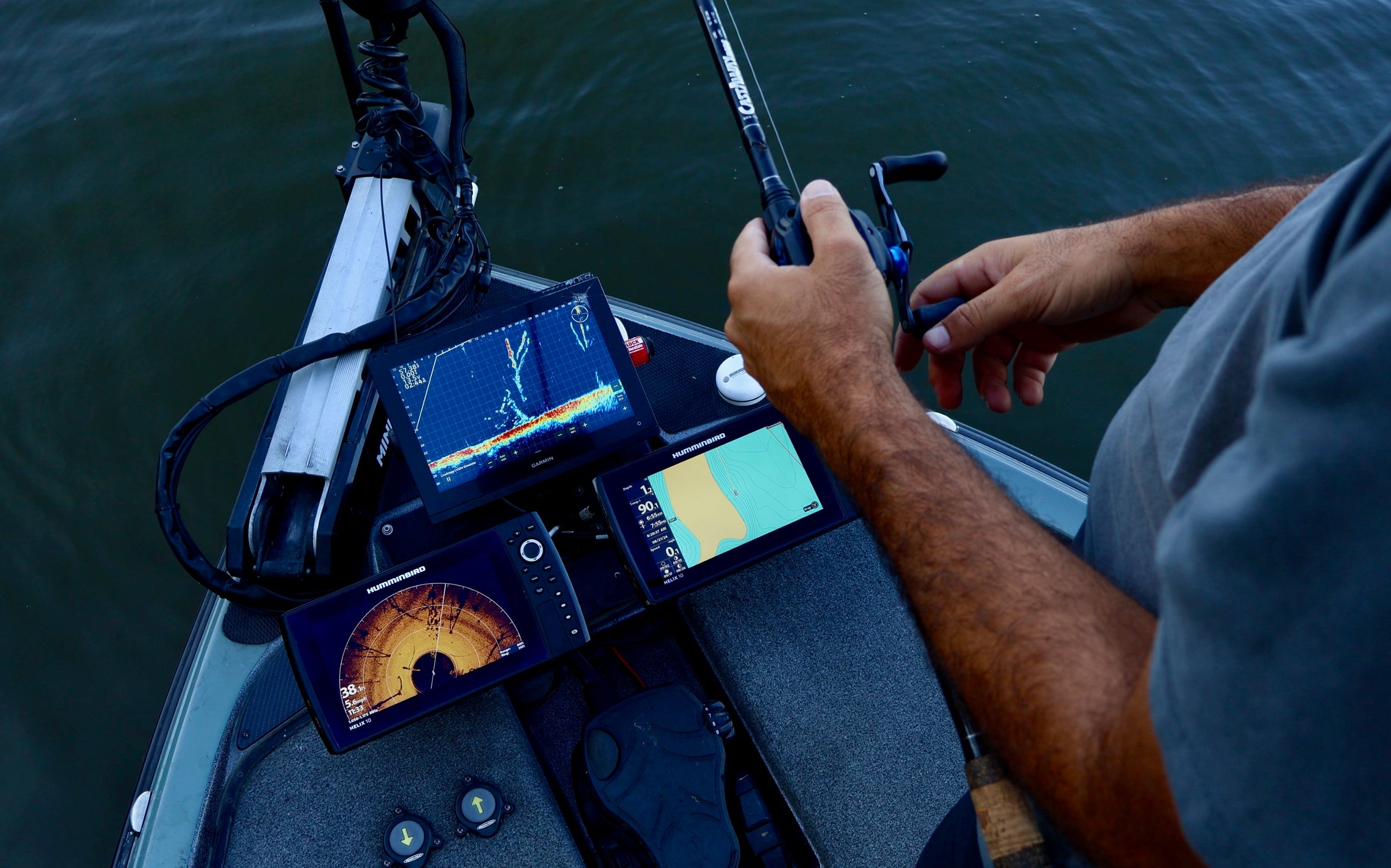 Angler using fish finder and sonar technology on a boat to locate underwater fish in calm waters.