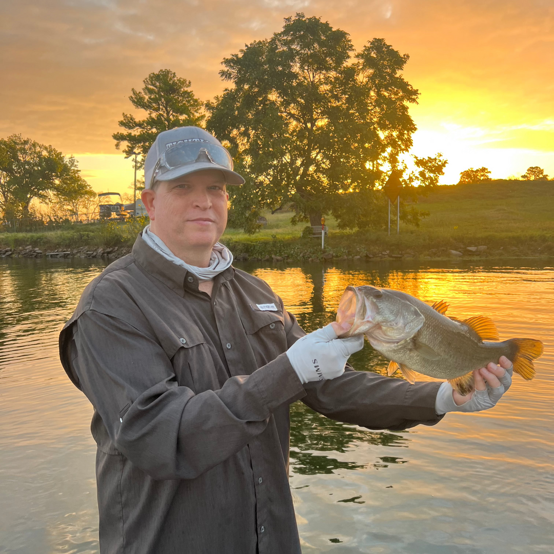 Man holding a bass with a sunrise in the background. 