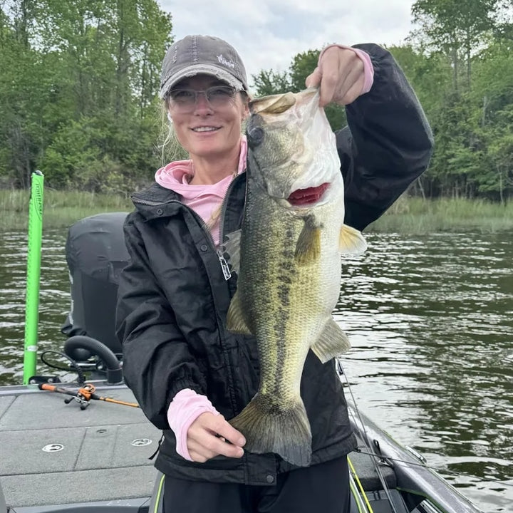 Woman in a black jacket holding a large bass fish while fishing on a lake.