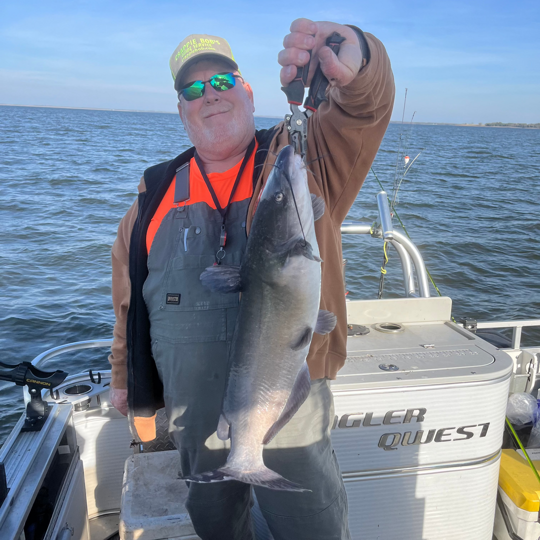 Man on a boat holding a big channel catfish with water in the background. 